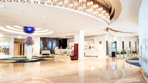 Een ruime lobby met een receptiebalie, een zithoek en een moderne kroonluchter.