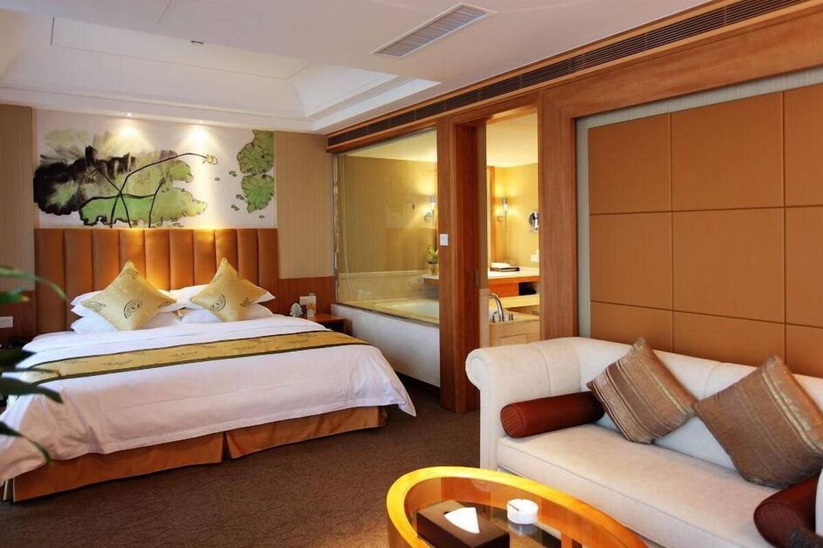 Une chambre d’hôtel avec un grand lit, un canapé, une petite table et une salle de bain visible à travers une porte ouverte.