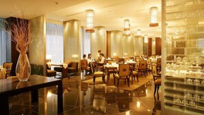 A well-lit dining area with tables and chairs, a decorative vase, and a glass display case with items. - Jinling Plaza Changzhou (Changzhou)