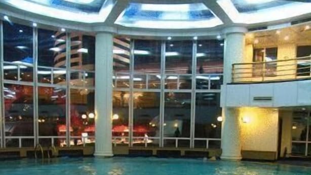 An indoor swimming pool with clear glass ceilings, a poolside area, and a view of the cityscape through large windows. - Jinling Plaza Changzhou (Changzhou)