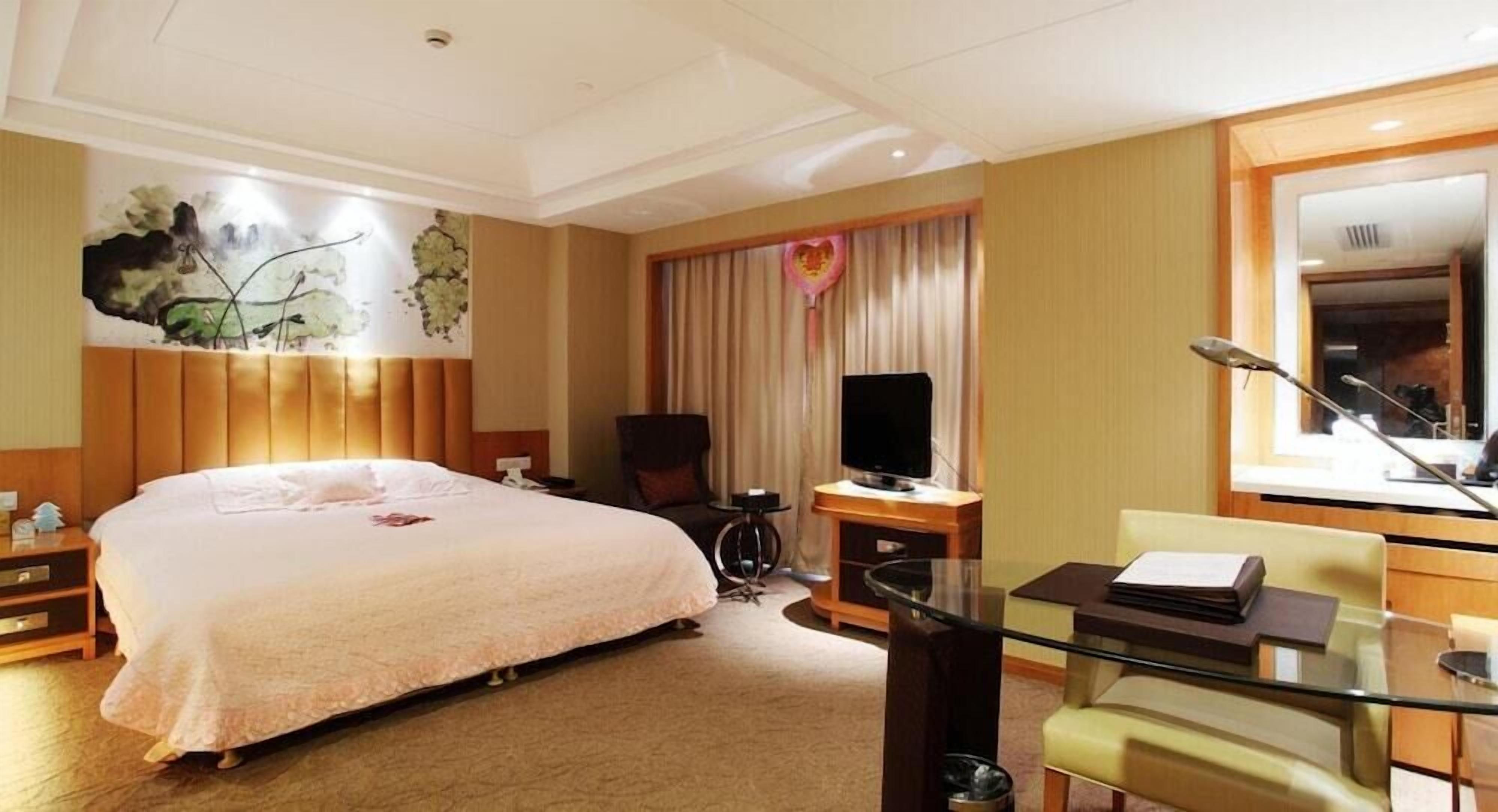 A hotel room with a large bed, a television, a desk with a chair, and a large mirror.
