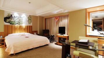 A hotel room with a large bed, a television, a desk with a chair, and a large mirror.