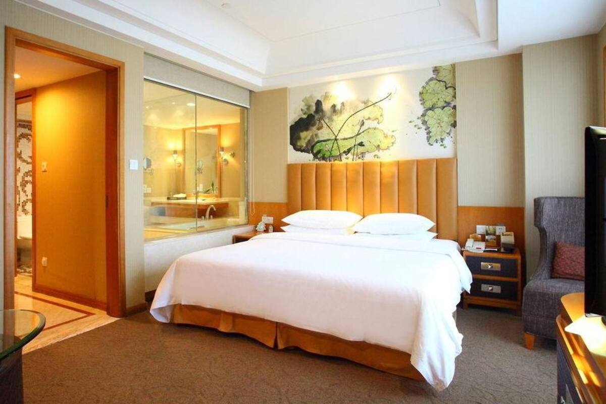 Une chambre d’hôtel avec un grand lit, une table de chevet, une chaise, un bureau et un miroir.