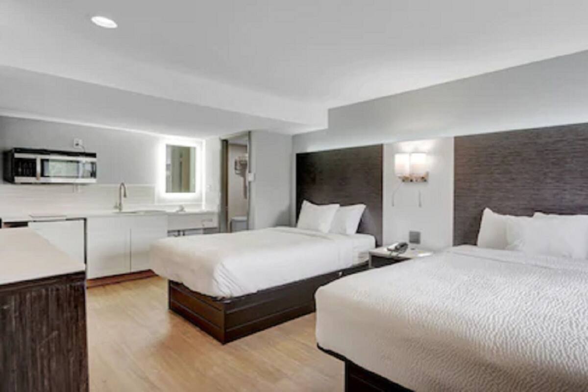 A hotel room with two beds, a kitchenette, and a bathroom.