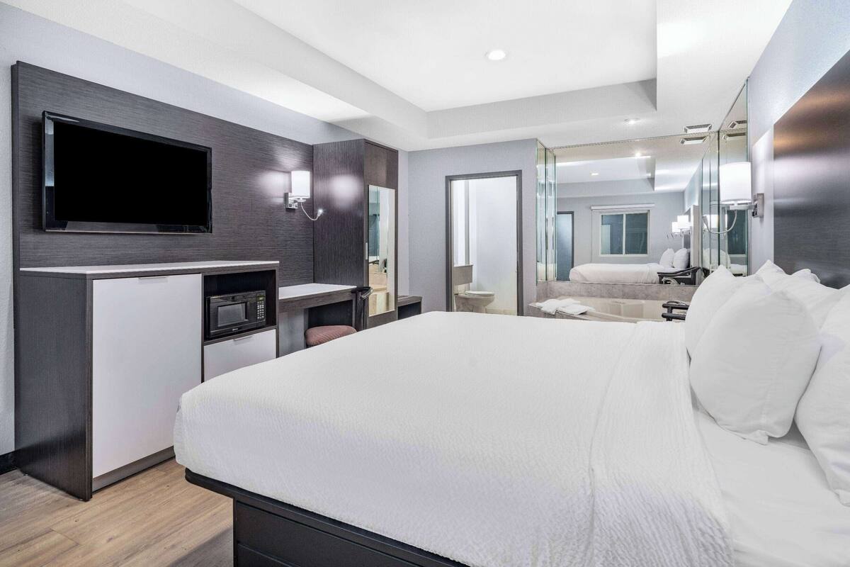 A modern hotel room with a large bed, a flat-screen TV, a microwave, and a small desk area.