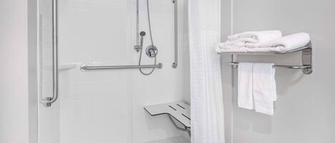 A shower area with a glass door, grab bars, a showerhead, and a towel rack with folded towels.