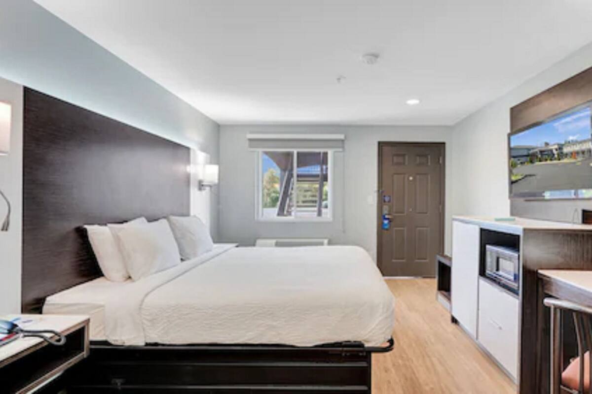 A modern hotel room with a bed, a desk, a TV, and a window with a view.