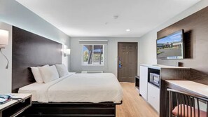 A modern hotel room with a bed, a desk, a TV, and a window with a view. - Days Inn & Suites by Wyndham Niagara Falls/Buffalo (Niagara Falls)