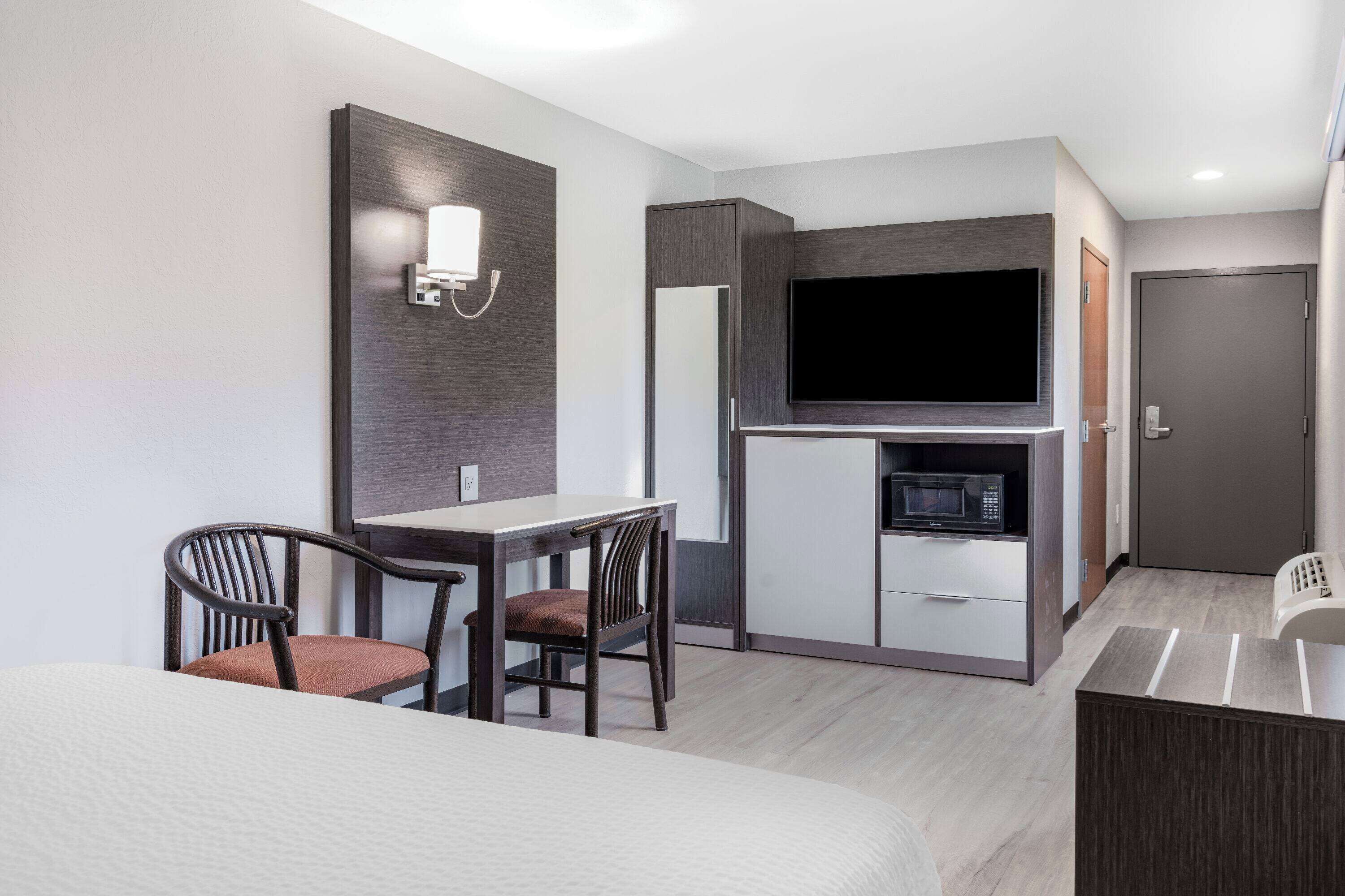 A modern hotel room with a bed, a desk with a chair, a flat-screen TV, a microwave, and a wardrobe.