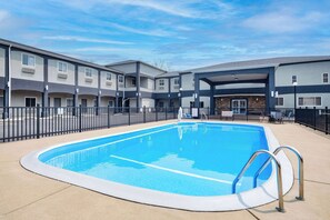 A swimming pool surrounded by a multi-story building with balconies and a covered area. - Days Inn & Suites by Wyndham Niagara Falls/Buffalo (Niagara Falls)