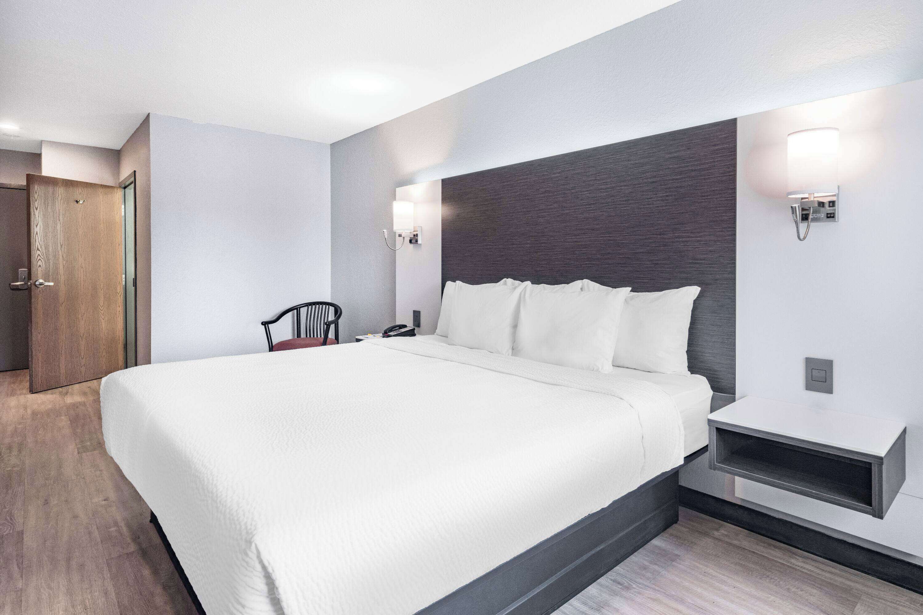 Ein modernes Hotelzimmer mit einem großen Bett, einem Nachttisch, einem Sessel und einer Holztür.