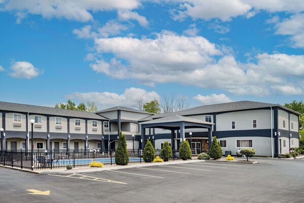A multi-story hotel with a covered entrance, a swimming pool, and a parking lot. - Days Inn & Suites by Wyndham Niagara Falls/Buffalo (Niagara Falls)