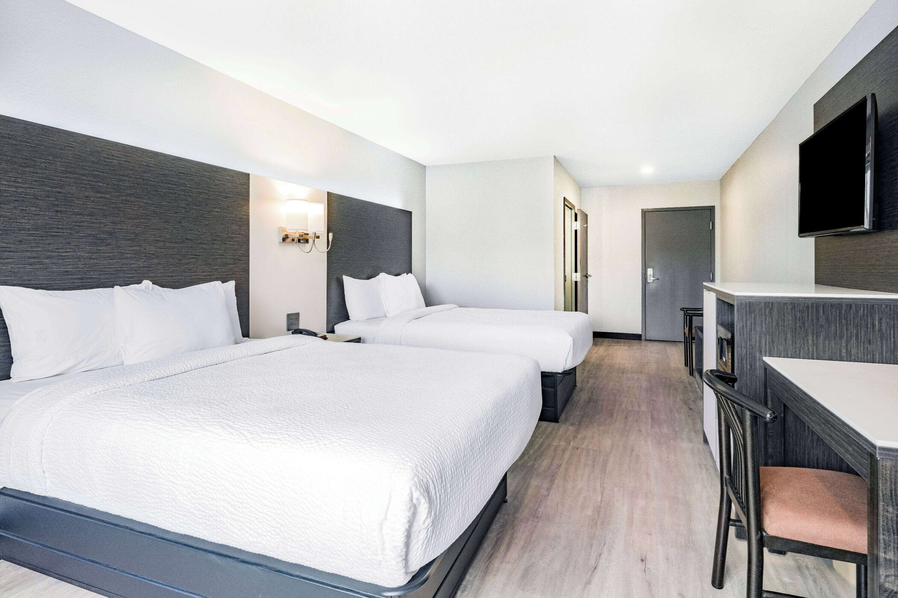A hotel room with two beds, a desk, and a TV.