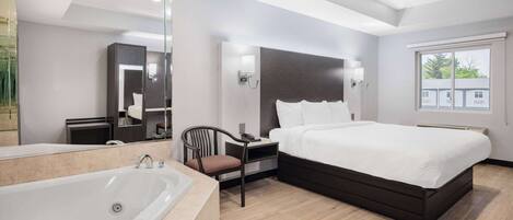 Quarto de hotel moderno com uma cama grande, banheiro separado com banheira, uma poltrona e uma mesinha de cabeceira.