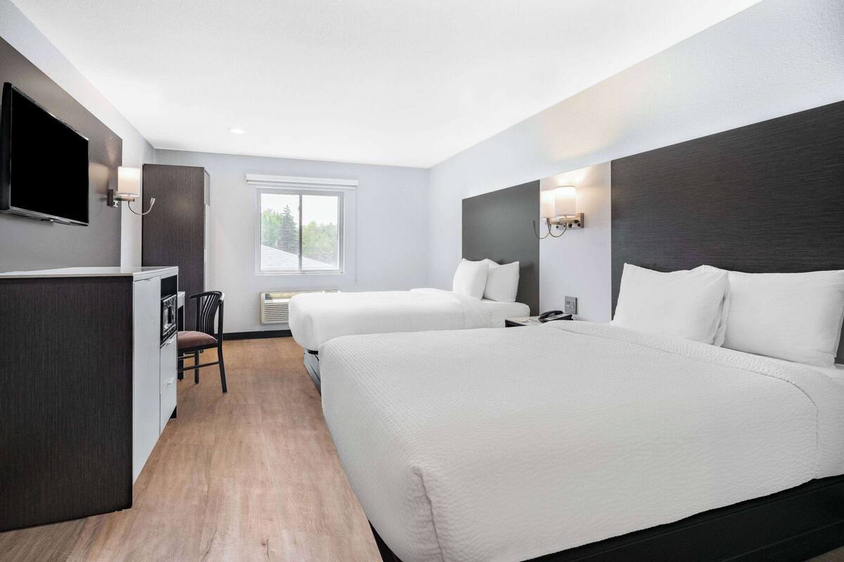 A hotel room with two beds, a TV, a desk, and a chair.