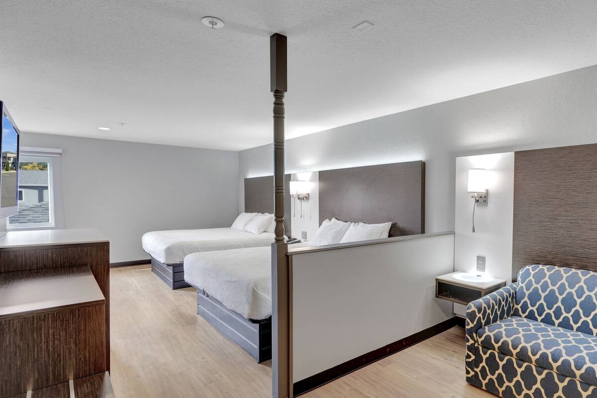 A hotel room with two beds, a desk, a sofa, and a bathroom.