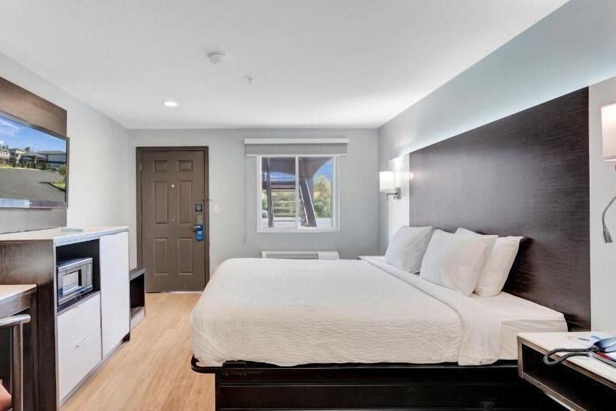 A modern hotel room with a bed, desk, TV, and a window with a view.