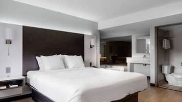 A modern hotel room with a large bed, a bedside table, a mirror, a bathroom with a toilet and sink, and a walk-in closet.