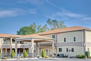 A multi-story hotel with a covered entrance, outdoor seating, and a parking lot. - Days Inn & Suites by Wyndham Niagara Falls/Buffalo (Niagara Falls)