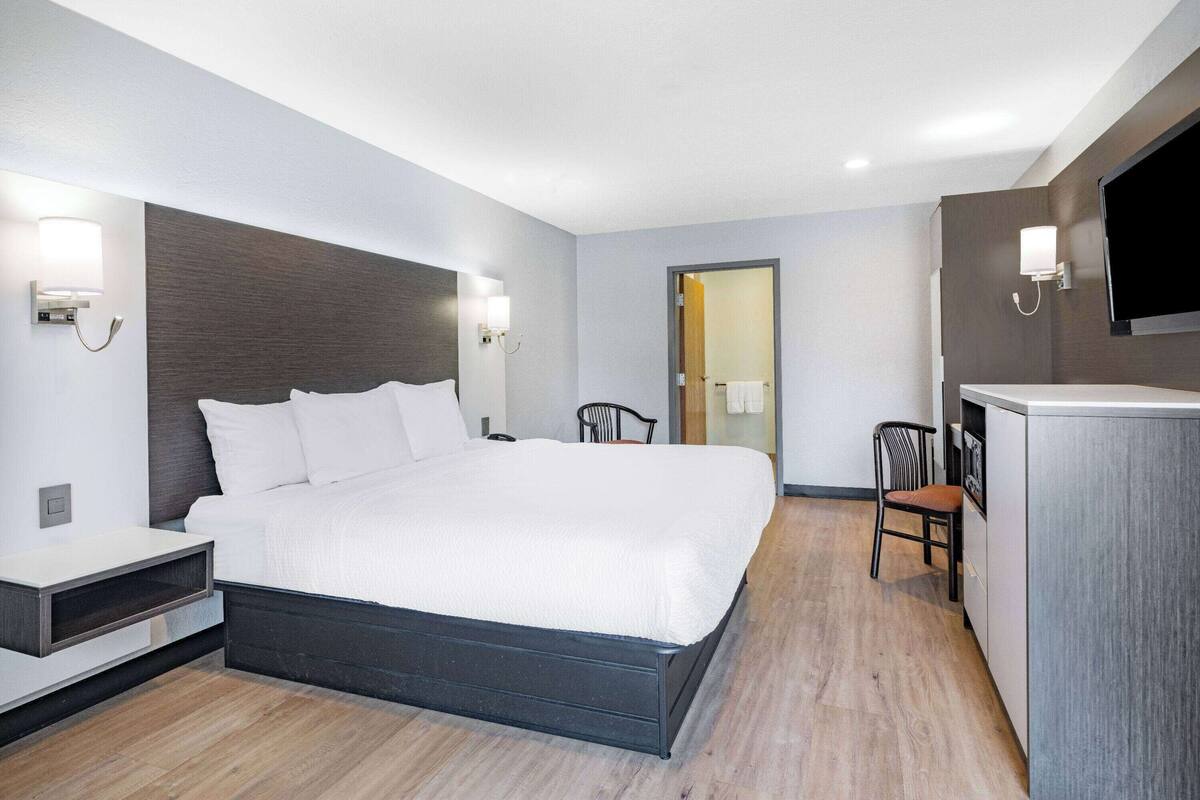 A modern hotel room with a large bed, bedside tables, a desk, and a TV.