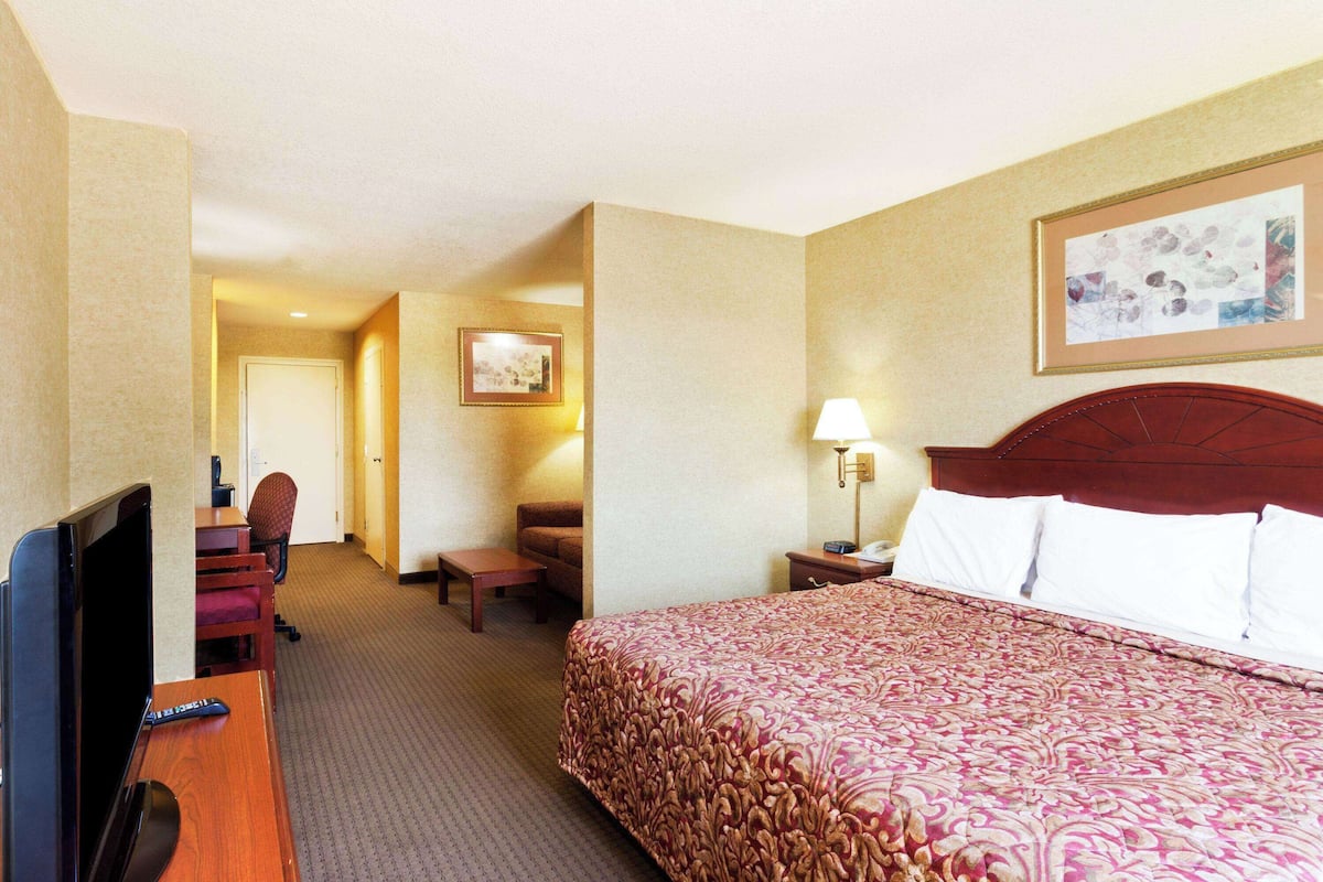 A hotel room with a large bed, a desk with a TV, a chair, a lamp, and a framed picture on the wall.