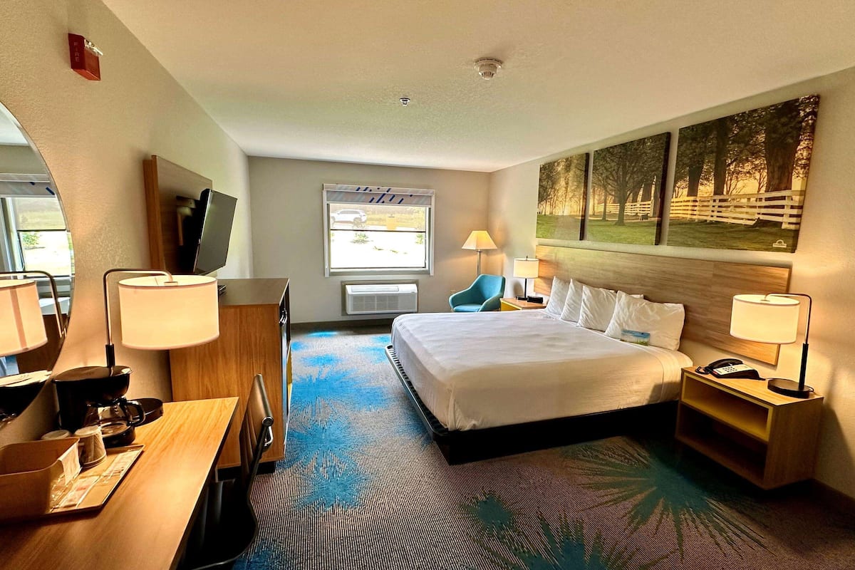 A hotel room with a bed, bedside tables, a desk with a chair, a TV, and a window with a view of the outside.