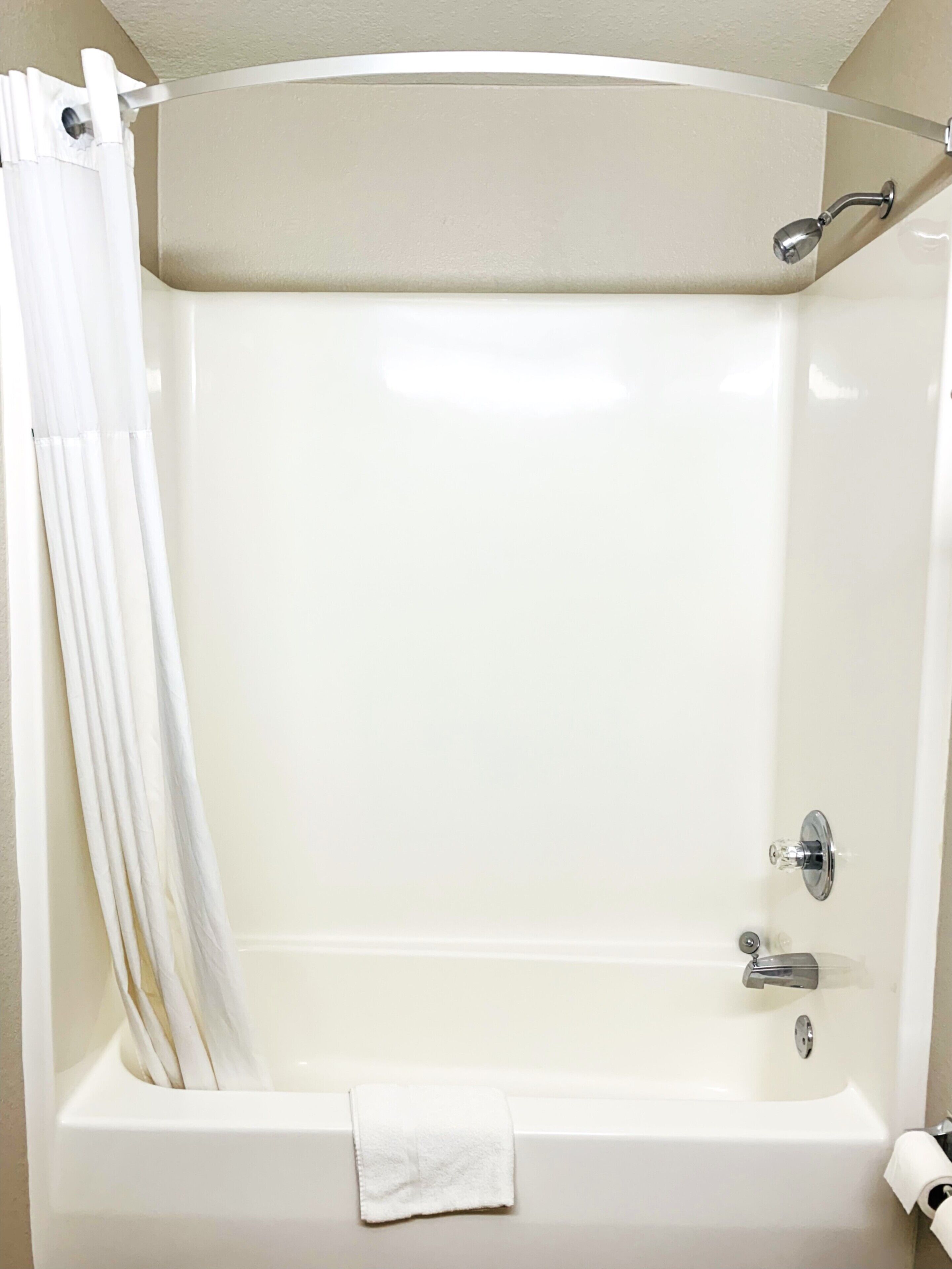 Una bañera blanca con cortina de ducha, una toalla y un rollo de papel higiénico.