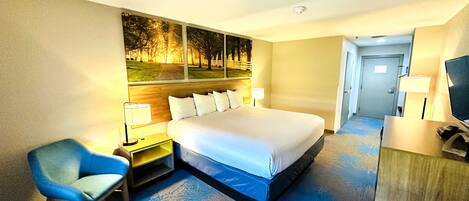Habitación de hotel con una cama grande, un escritorio con silla, un televisor y un cuadro de árboles.