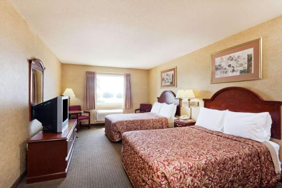 A hotel room with two beds, a TV, a desk, and a window with curtains.