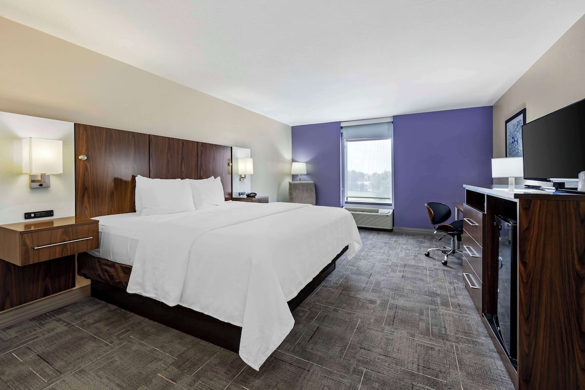 A hotel room with a large bed, a desk with a chair, a television, and a window with a view.