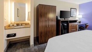 A hotel room with a bed, a wooden wardrobe, a television, a desk with a lamp, and a bathroom with a sink and mirror. - Best Western Gen X Inn (Memphis)