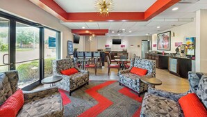 A hotel lobby with patterned sofas, a bar area, and a view through large windows. - Best Western Gen X Inn (Memphis)