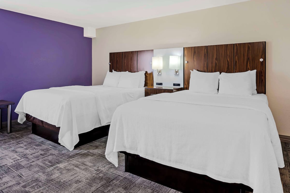 A hotel room with two beds, a nightstand, and a small table.