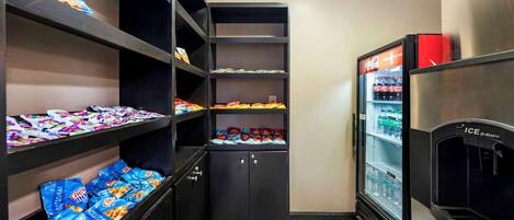 Una kitchenette pequeña con estantes llenos de aperitivos y un refrigerador.