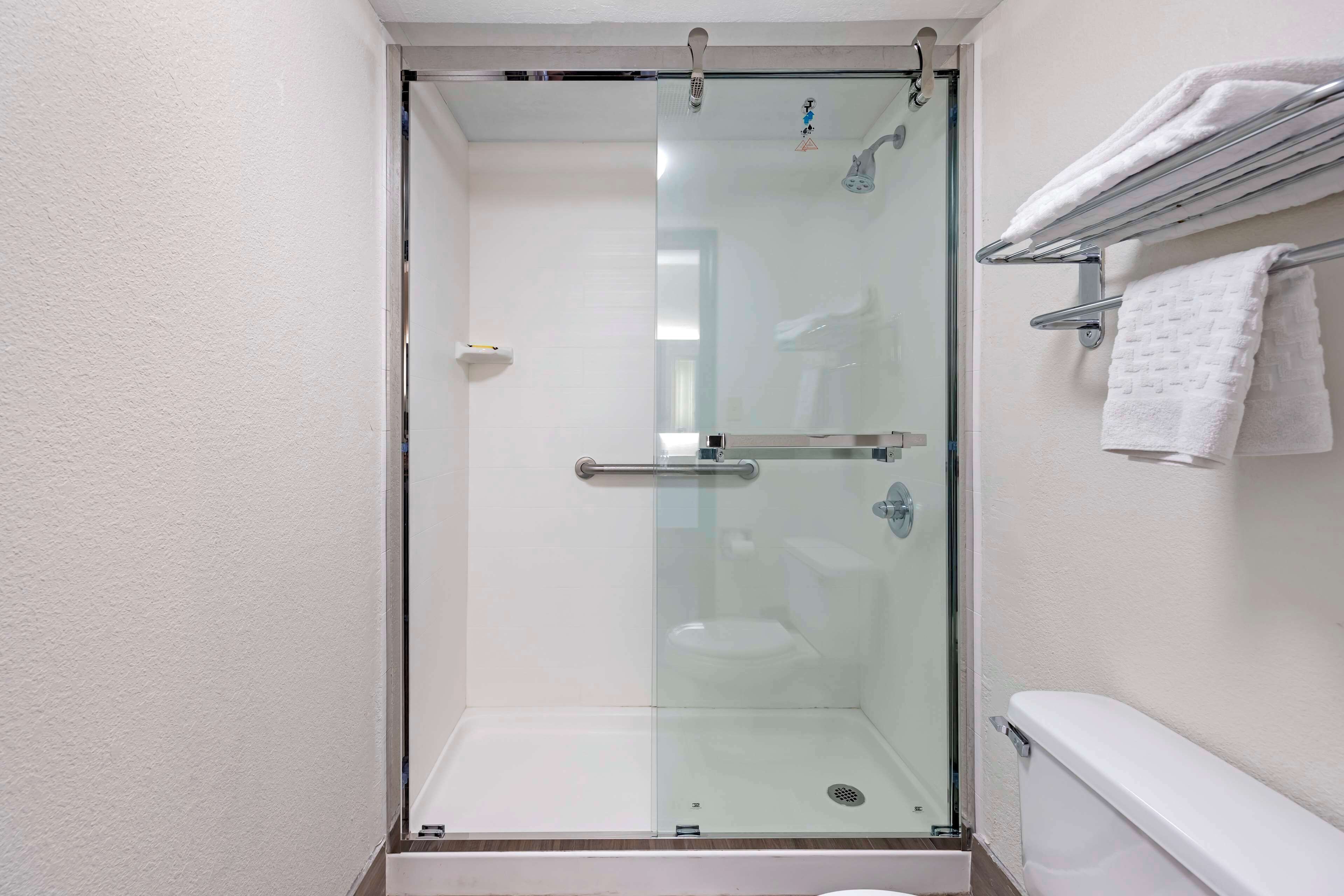 Een douchecabine met glazen wanden, een wit toilet en een handdoekhouder erboven.