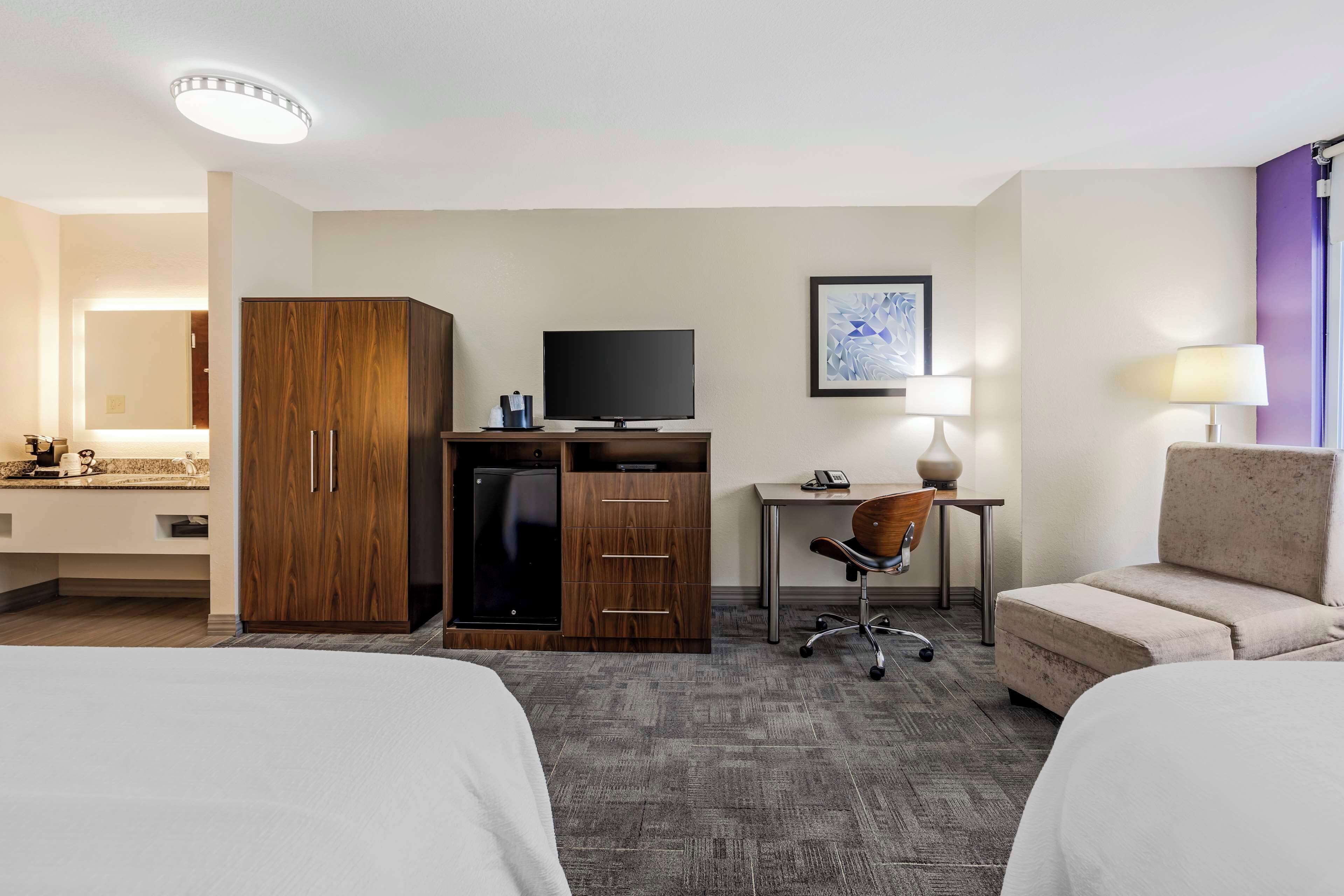 A hotel room with two beds, a desk with a chair, a television, a wardrobe, and a framed picture on the wall.
