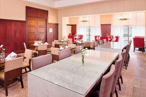 Un comedor de hotel con una gran mesa de mármol, sillas tapizadas en rojo y una puerta de madera.