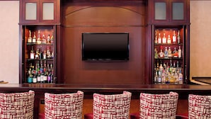 A bar area with a flat-screen TV, shelves of liquor bottles, and patterned bar stools.