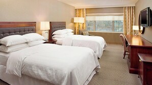 A hotel room with two beds, a desk, a chair, a TV, and a window with curtains.