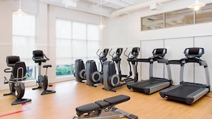 A gym with various exercise equipment, large windows, and a wooden floor.