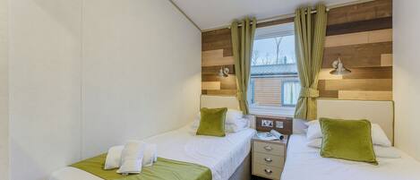 A hotel room with two single beds, a wooden headboard, a nightstand, and a window with curtains.