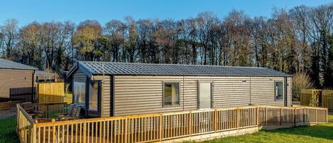 A mobile home with a deck, a small patio, and a window overlooking a grassy area.