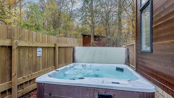 A hot tub in a wooden cabin setting with a wooden deck and trees in the background.