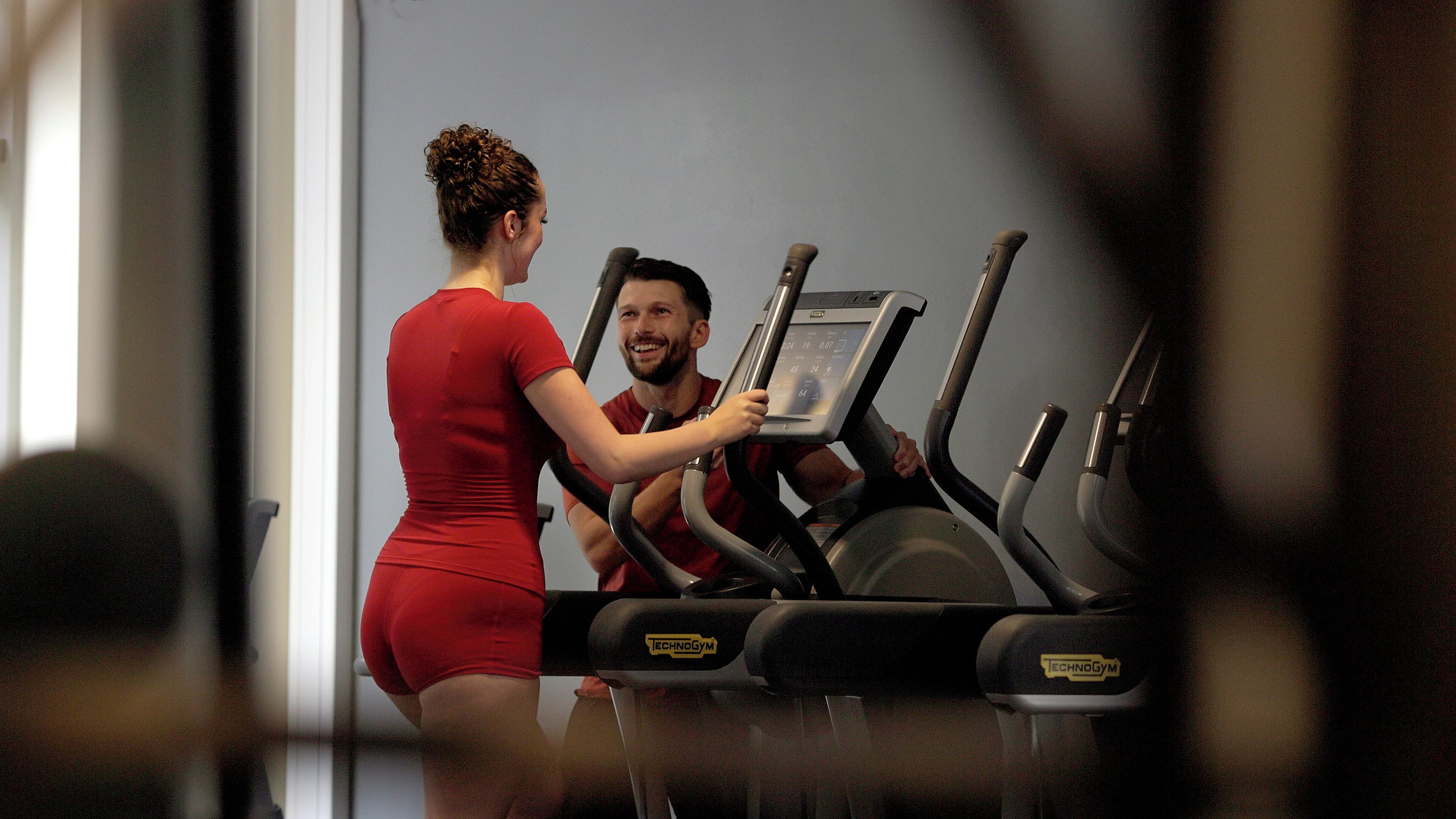 Un gimnasio con cintas de correr y una persona usándola.