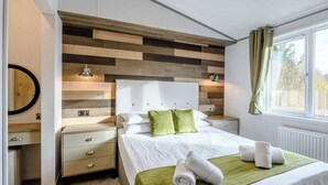 Een keurig opgemaakt slaapkamer met een bed, nachtkastjes, een kaptafel en een raam met gordijnen.