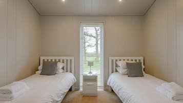 Ein Schlafzimmer mit zwei Betten, einem Fenster mit Jalousien und einem Nachttisch mit Lampe.