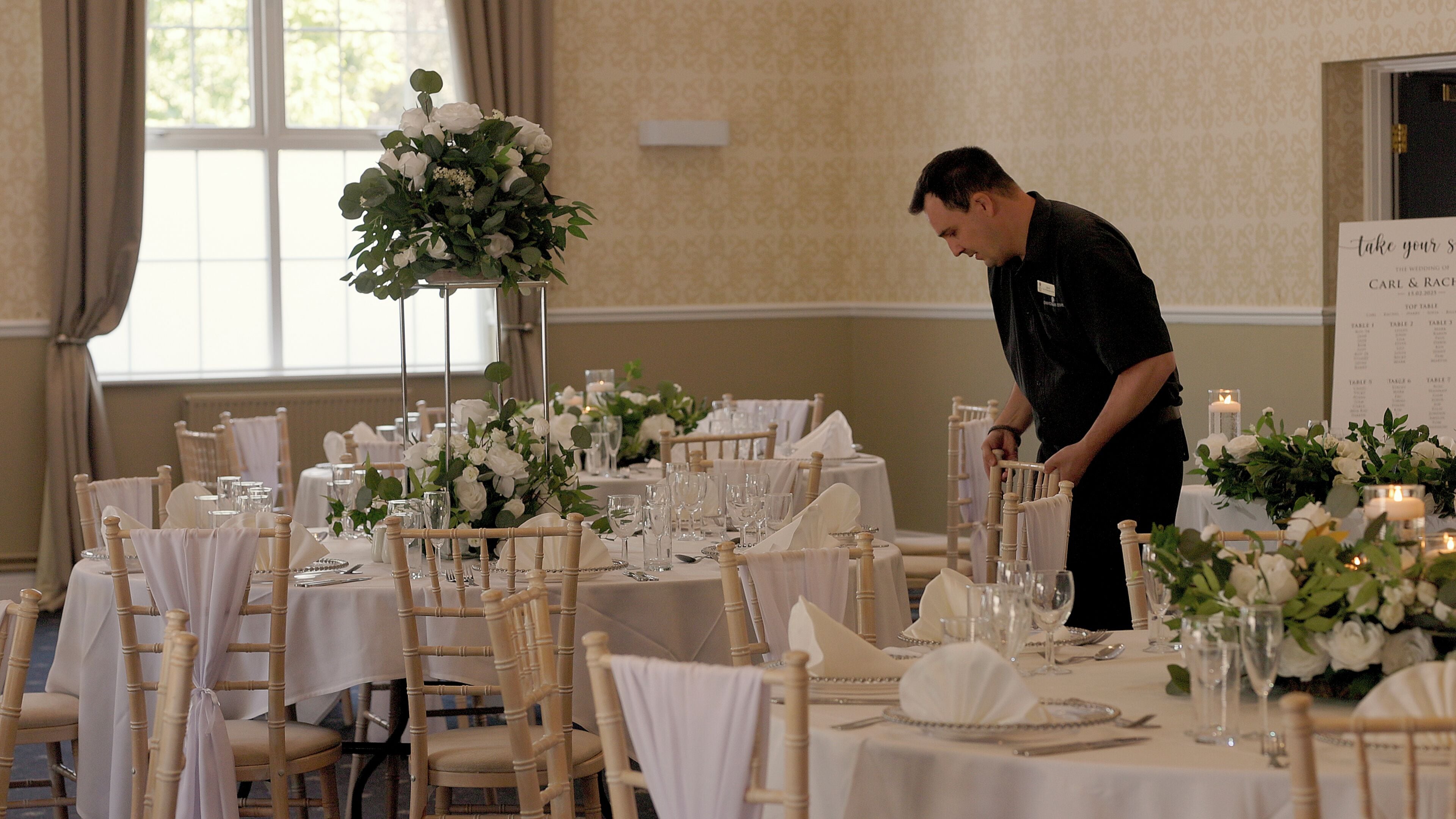 Un salón de banquetes con mesas dispuestas para un evento formal, destacando manteles blancos, centros de mesa florales y cristalería impecable.