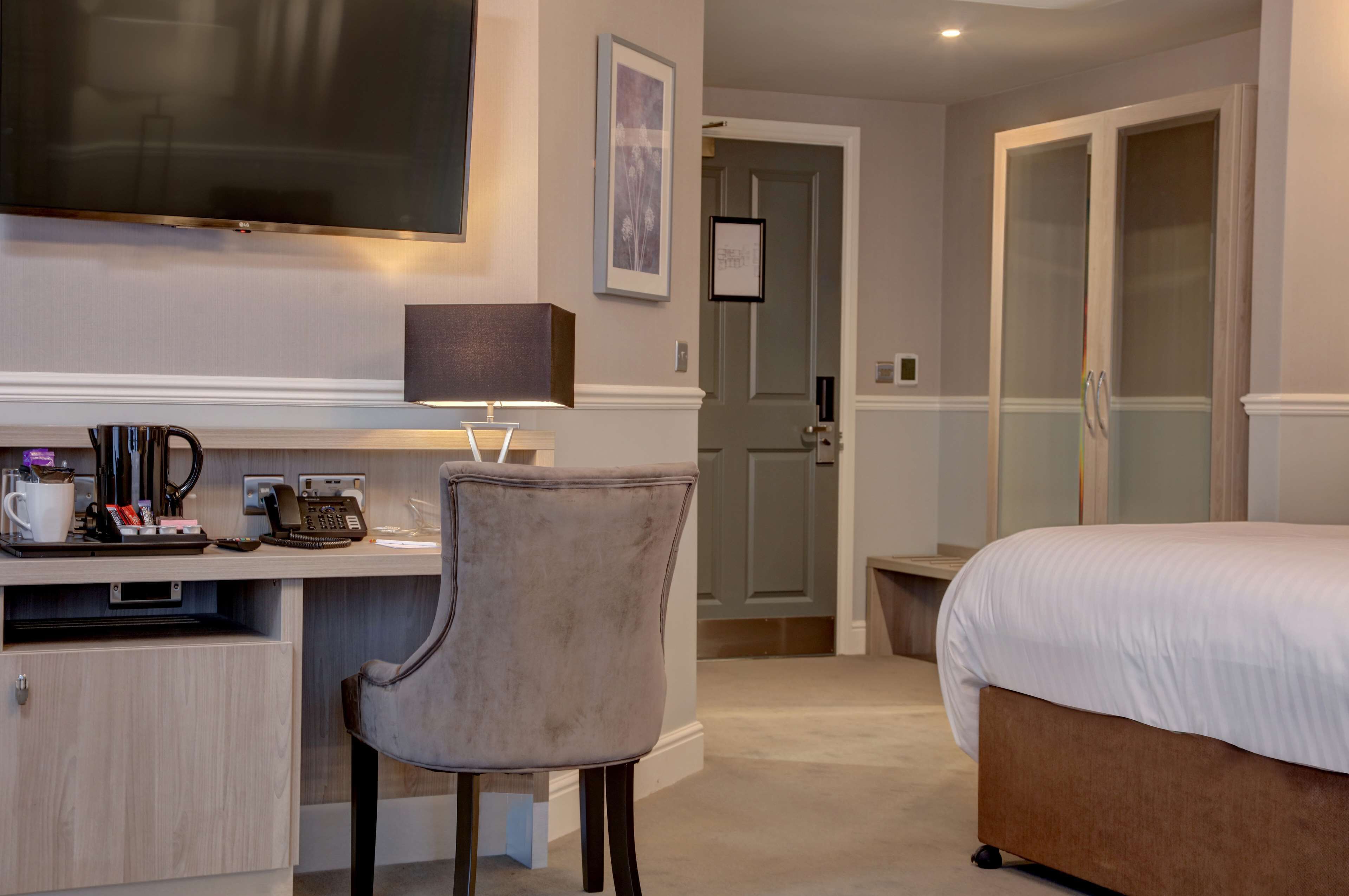 Ein Hotelzimmer mit Bett, Schreibtisch mit Lampe, Stuhl, Fernseher und einer Tür zum Badezimmer.