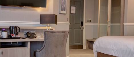A hotel room with a bed, a desk with a lamp, a chair, a TV, and a door leading to a bathroom.