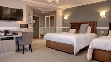 A hotel room with a large bed, a desk with a chair, a television, and a chandelier.